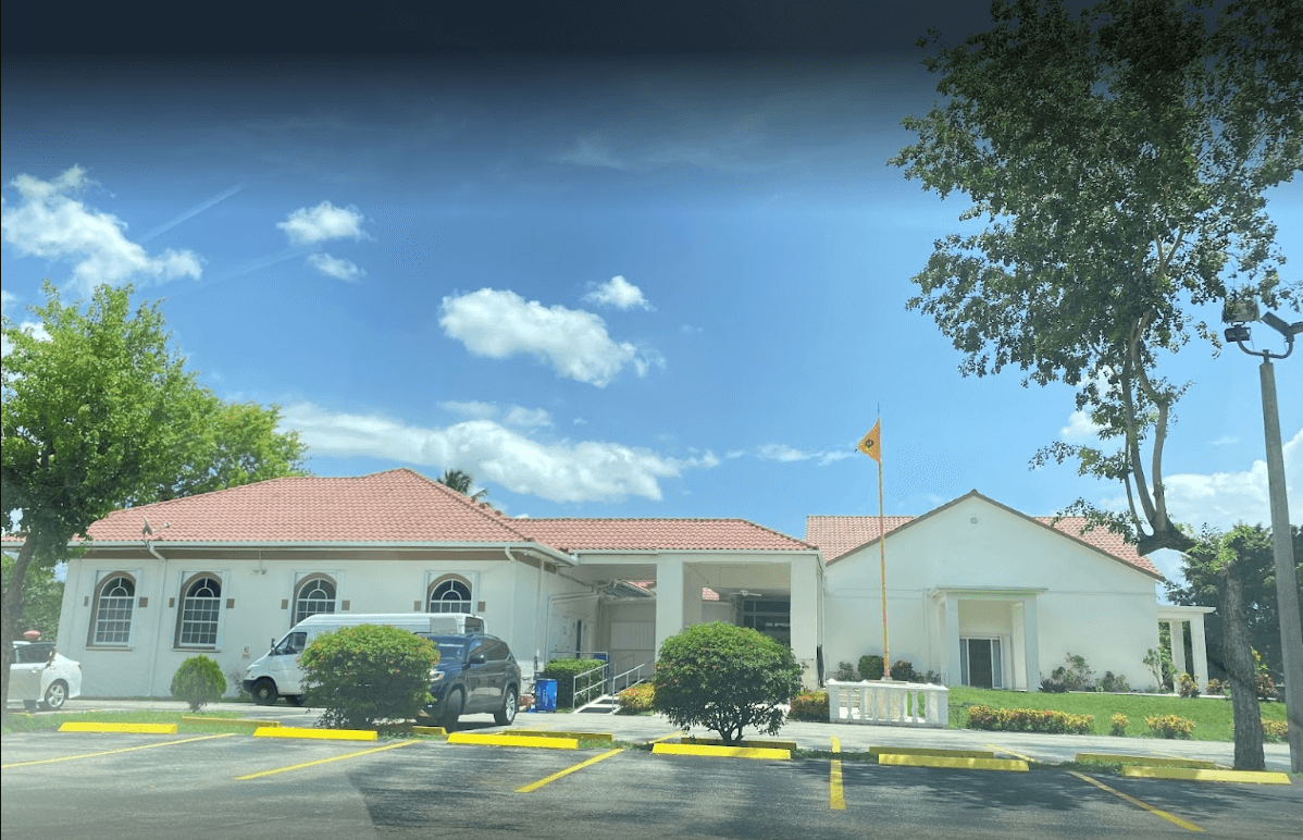 Sikh Society of Florida Gurdwara building with the Nishan Sahib flag under a blue Florida sky